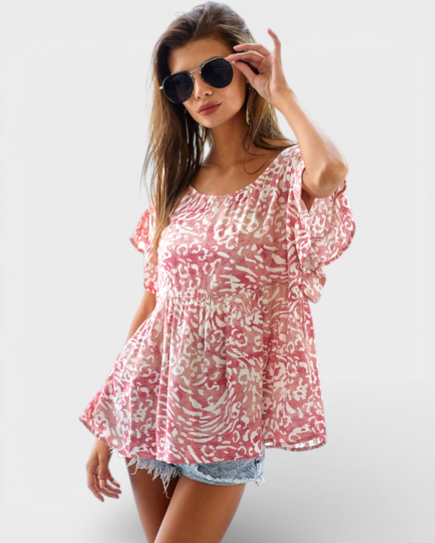 Woman wearing a pink and white patterned top with sunglasses on a white background