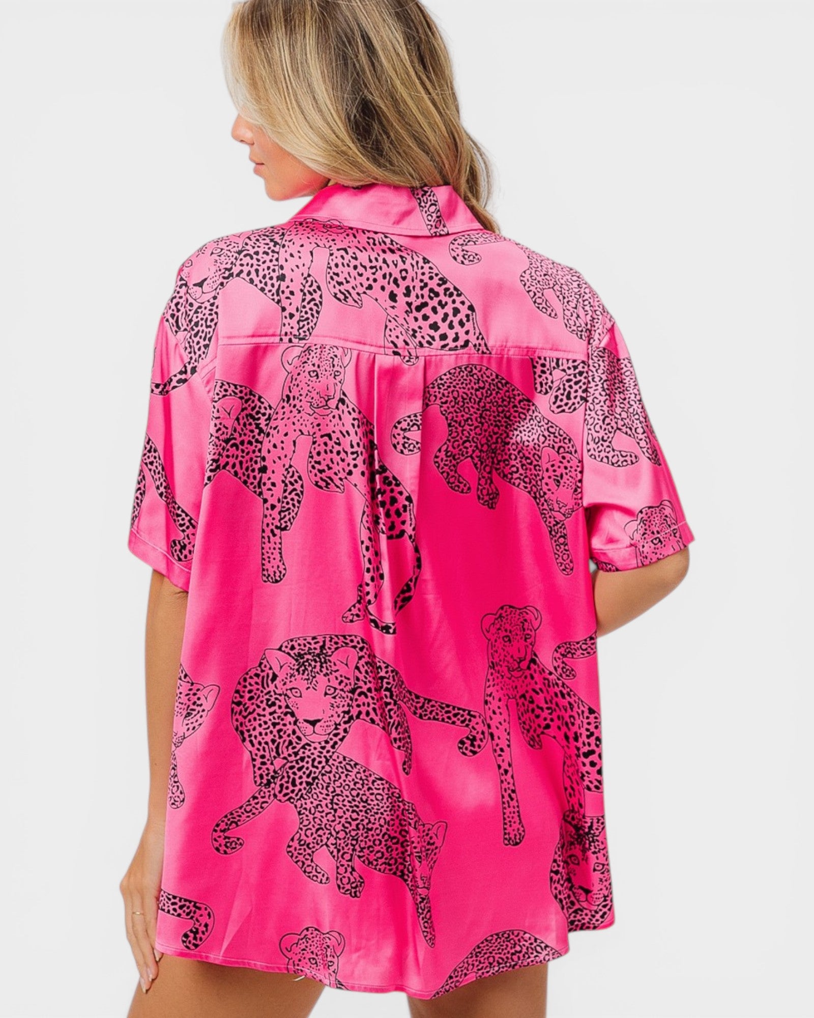 Woman wearing a pink satin shirt with black leopard print patterns on a white background