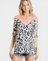 Woman wearing a leopard print top with pink trim and denim shorts on a white background