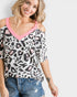 Woman wearing a leopard print top with pink trim and denim jeans on a white background