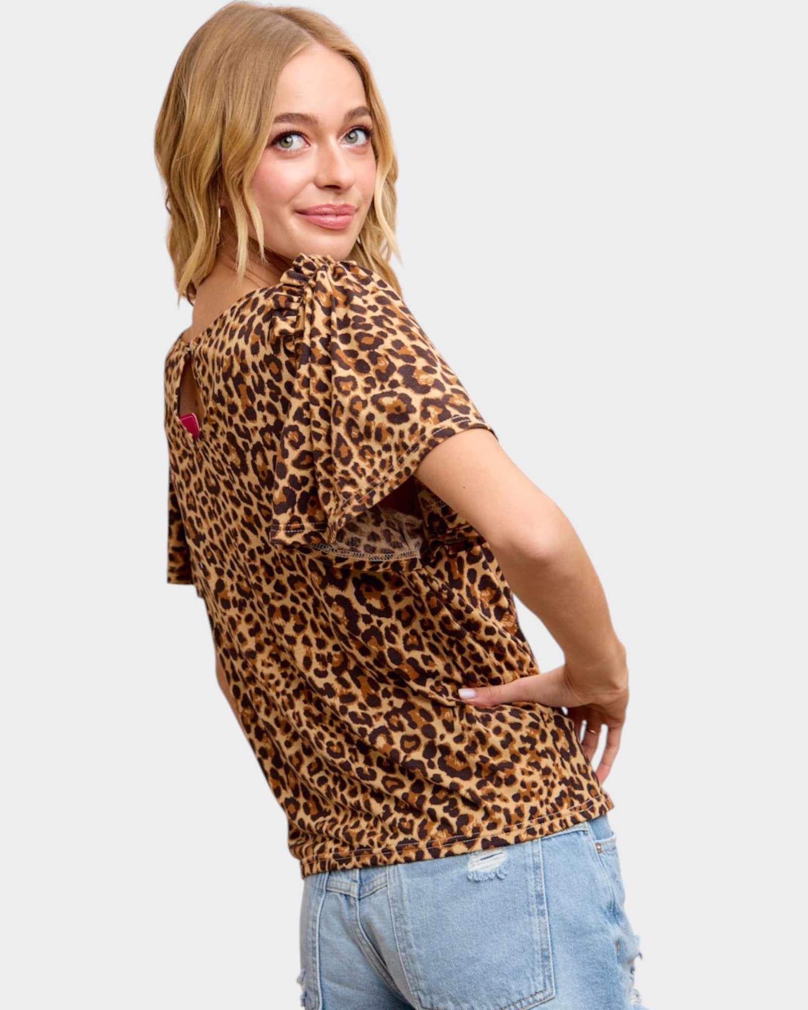 Woman wearing a leopard print top and blue jeans on a light gray background