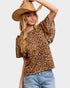 Woman wearing a leopard print top and denim shorts with a beige hat on a plain background