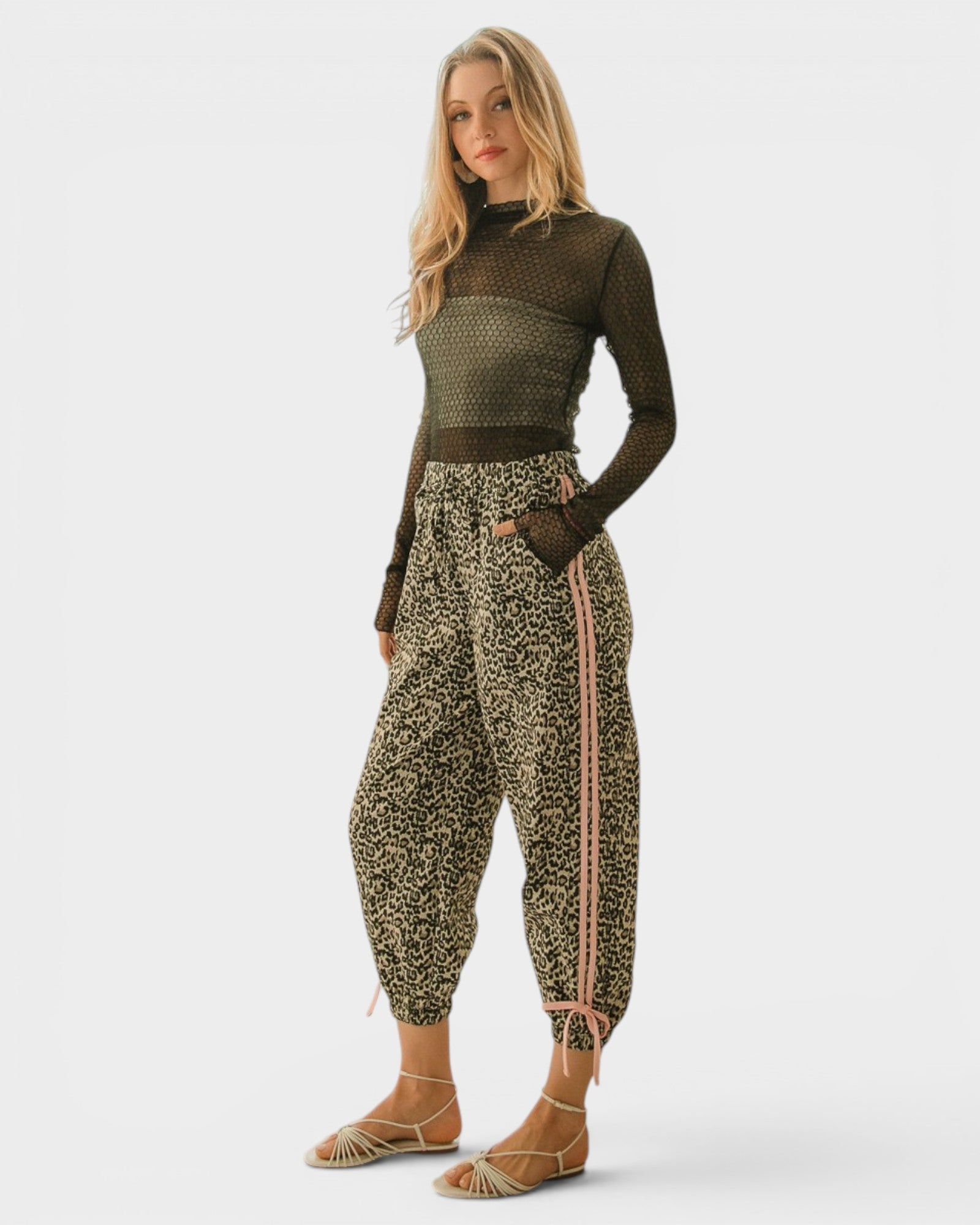 Woman wearing a green patterned top and high-waisted pants with a white background