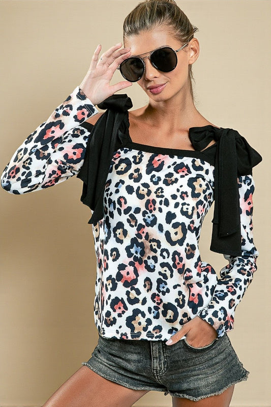 Woman wearing a leopard print top with floral accents and denim shorts against a beige background