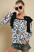 Woman wearing a leopard print top with floral accents and denim shorts against a beige background