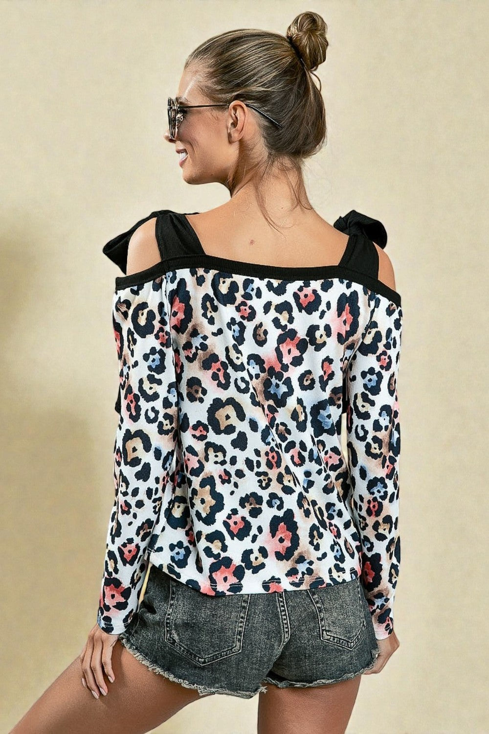 Woman wearing a leopard print top with black shoulder straps on a beige background