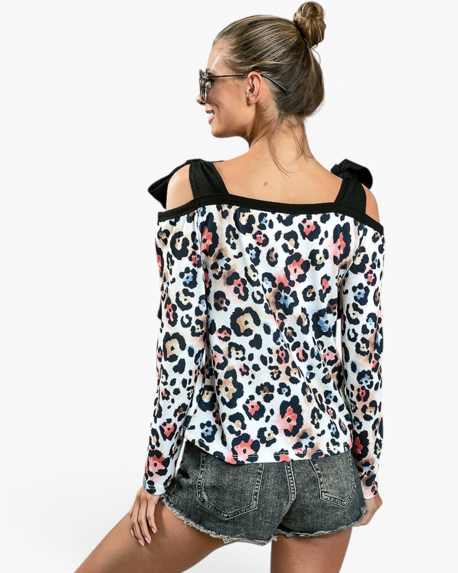 A woman shown from the back wearing a long-sleeve off-the-shoulder top with a black, pink, and blue leopard print on a white background, paired with gray denim shorts, against a plain white studio background.