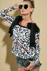 Woman wearing a leopard print top with black bows and denim shorts against a beige background