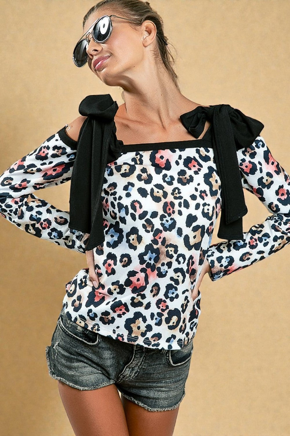 Woman wearing a leopard print top with black bows and denim shorts on a beige background