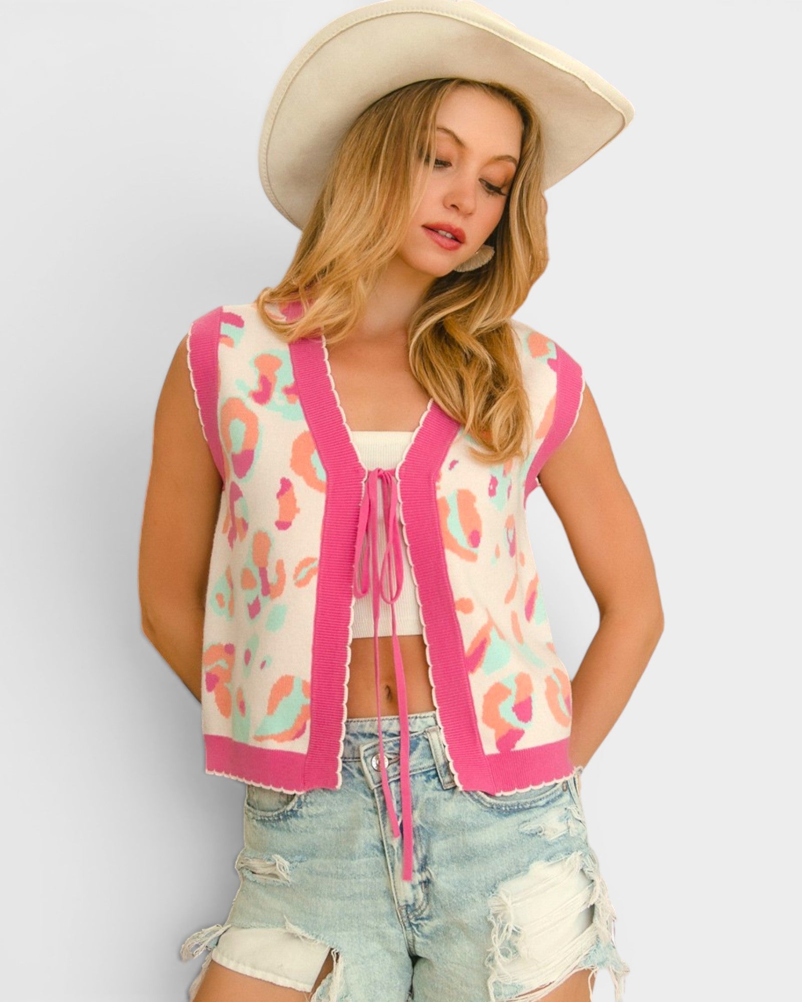 Woman wearing a patterned cardigan, shorts, and a cowboy hat on a plain background