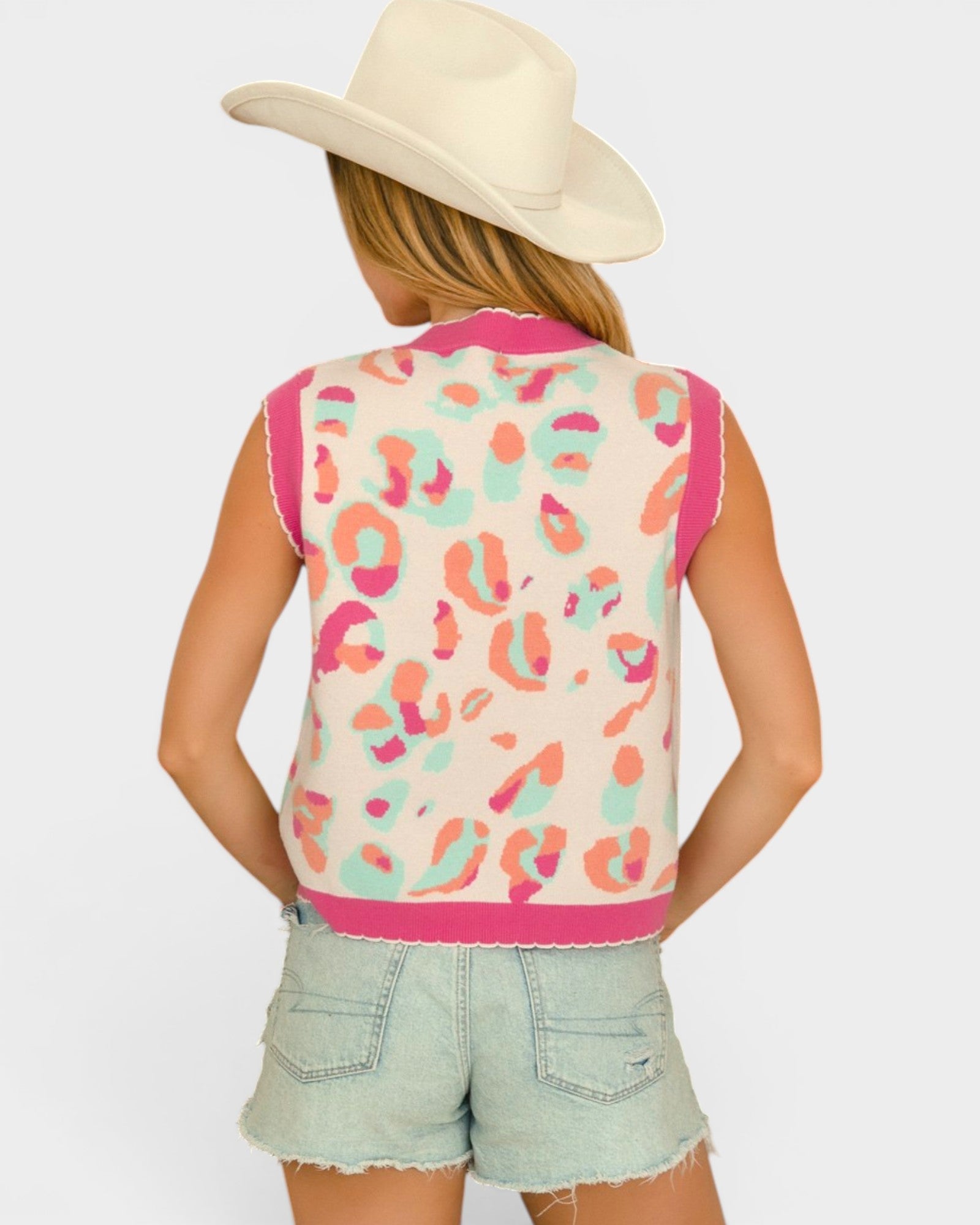 Person wearing a colorful leopard print vest and light denim shorts on a white background