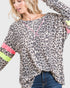 Woman wearing a leopard print top with colorful sleeves on a plain background