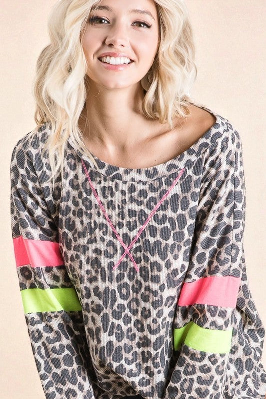 Woman wearing a leopard print top with colorful sleeves on a beige background