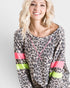 Woman wearing a leopard print top with colorful sleeves against a plain background