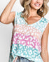 A woman wearing a sleeveless V-neck top with a pastel leopard print pattern in mint green, pink, peach, and white, paired with blue jeans and a tan hat against a light gray background.