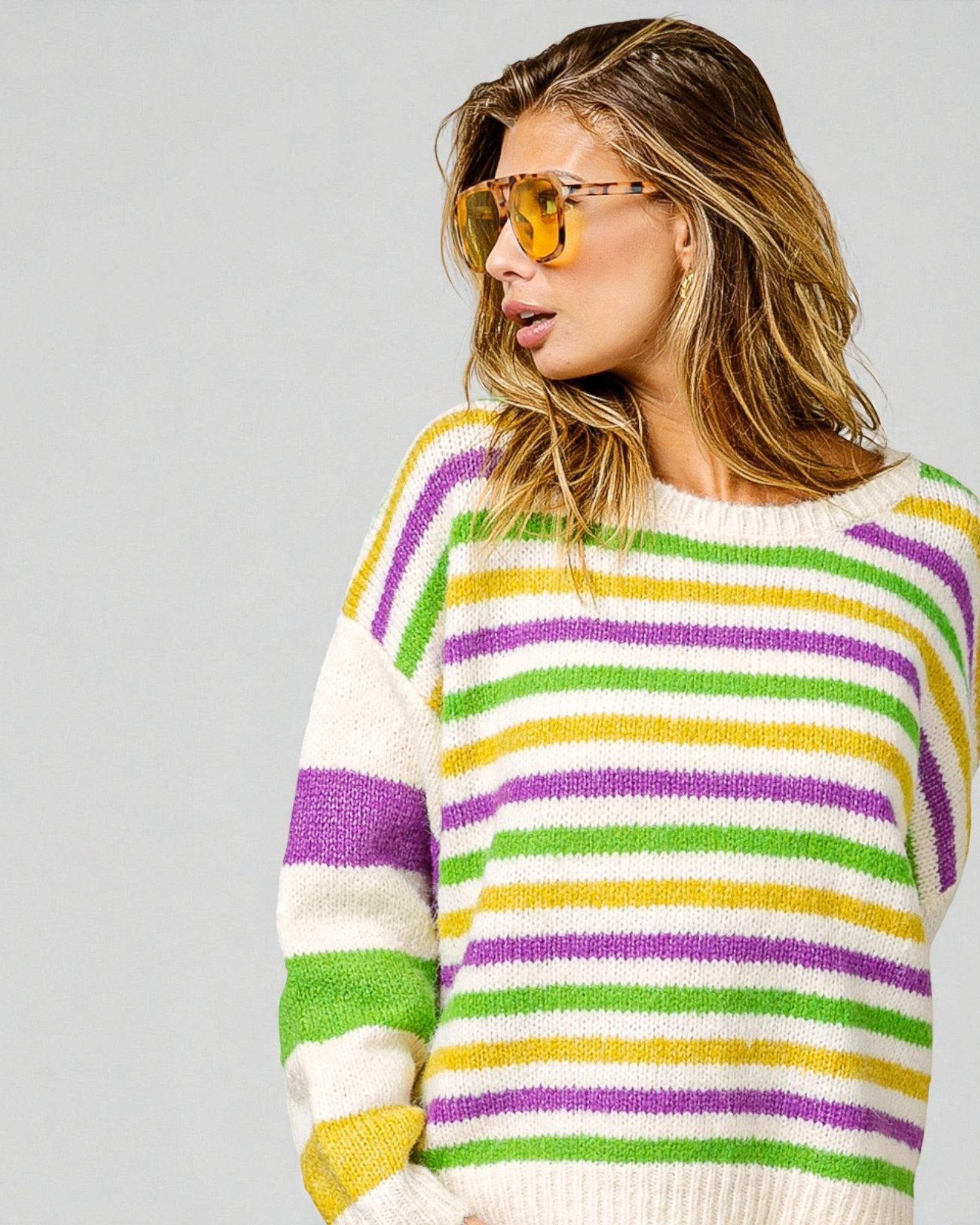 Woman wearing a colorful striped sweater and yellow sunglasses on a gray background