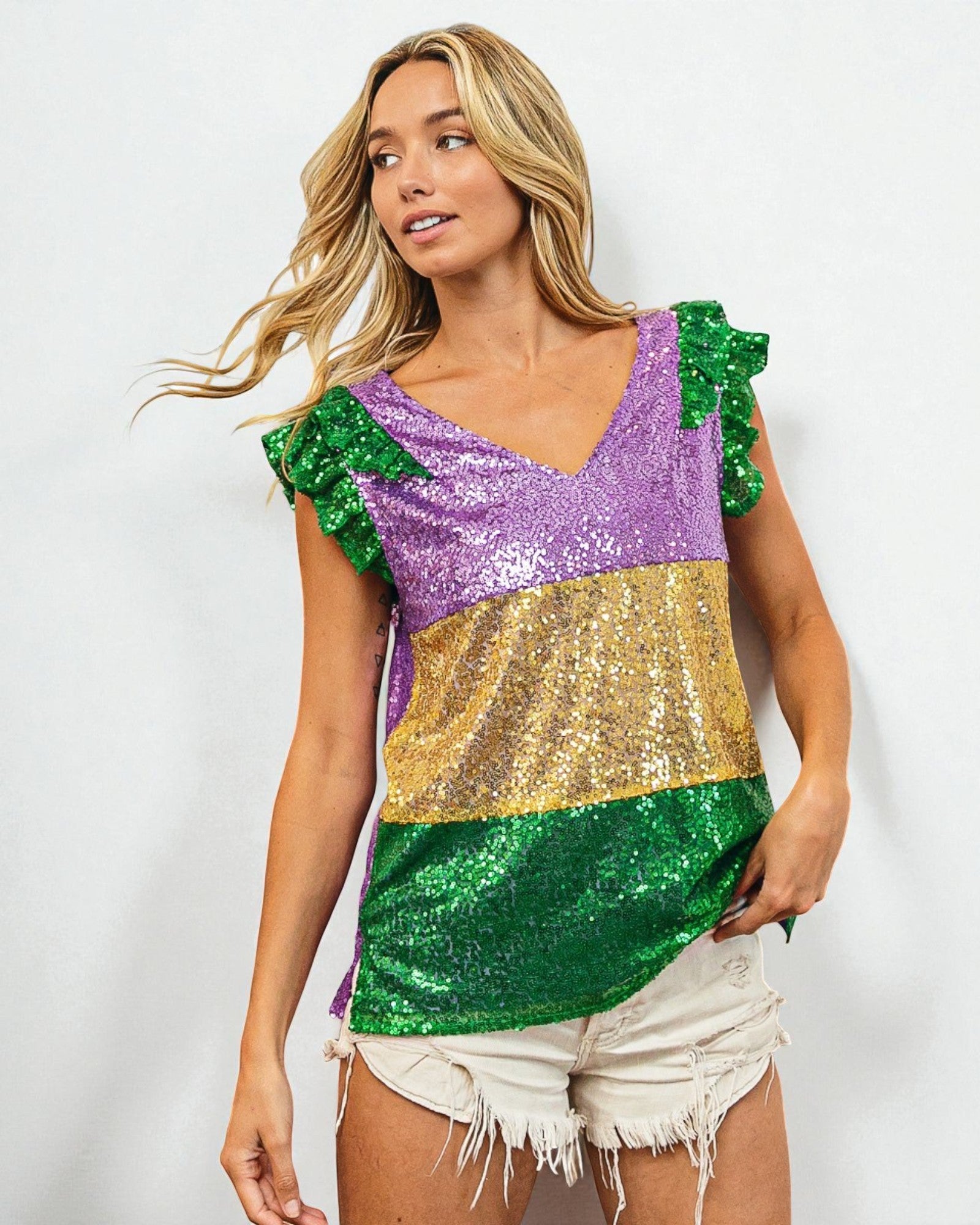Woman wearing a colorful sequin top with green, purple, and gold in front of a white background