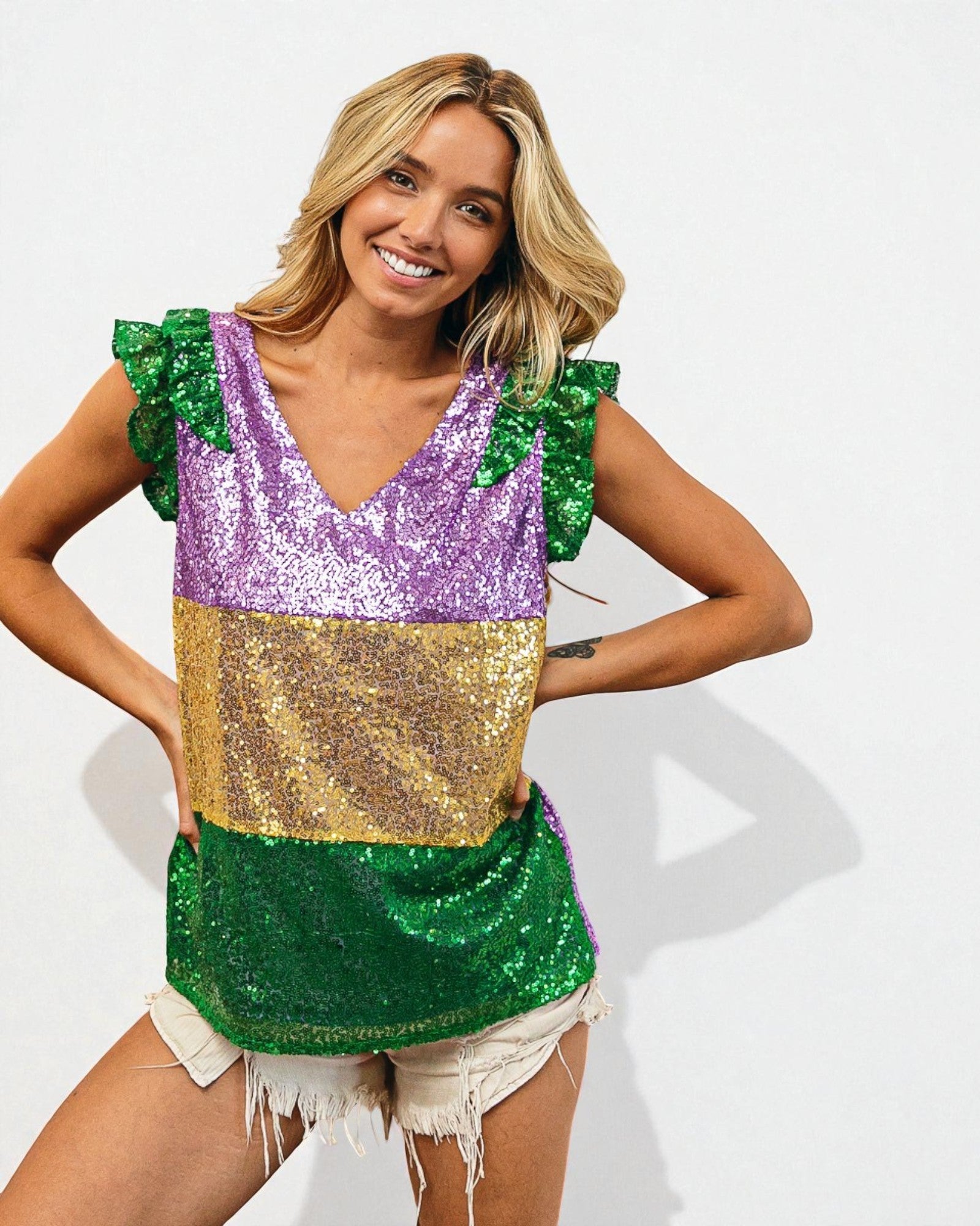 Woman wearing a colorful sequin top with green, purple, and gold sections on a white background