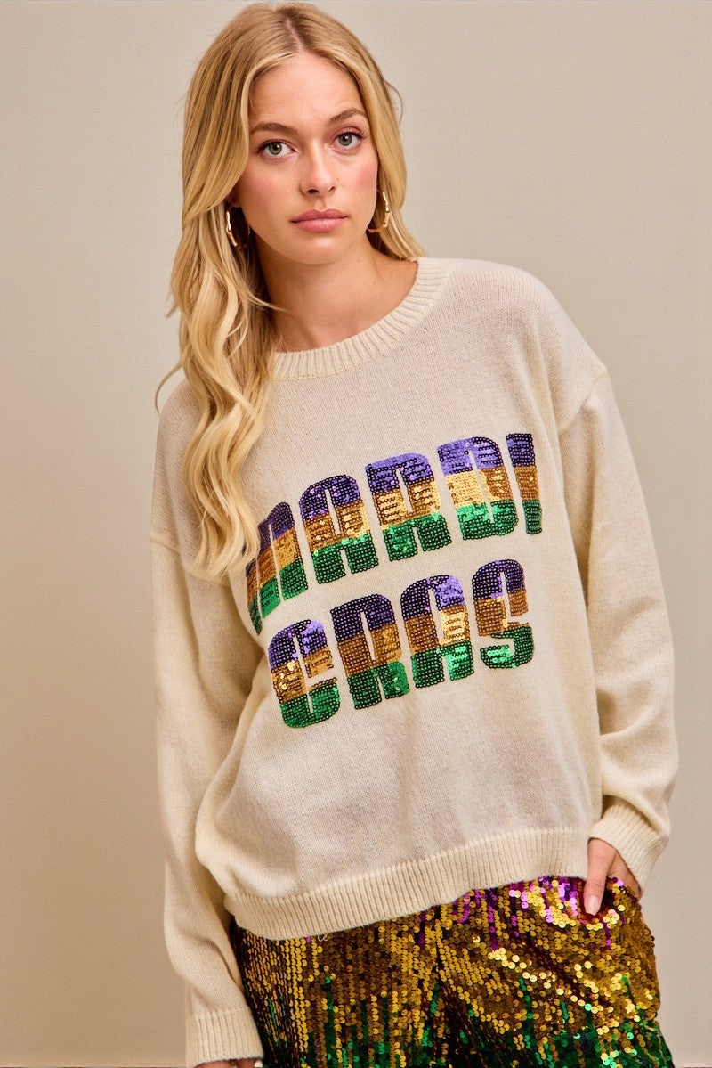 Woman wearing a cream sweater with colorful sequin text against a beige background