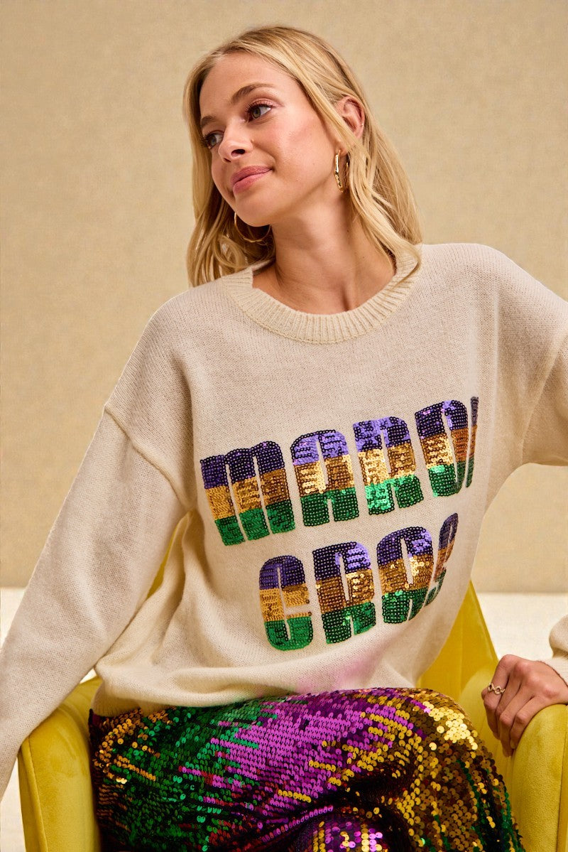 Woman wearing a beige sweater with colorful sequin letters, sitting on a yellow chair.