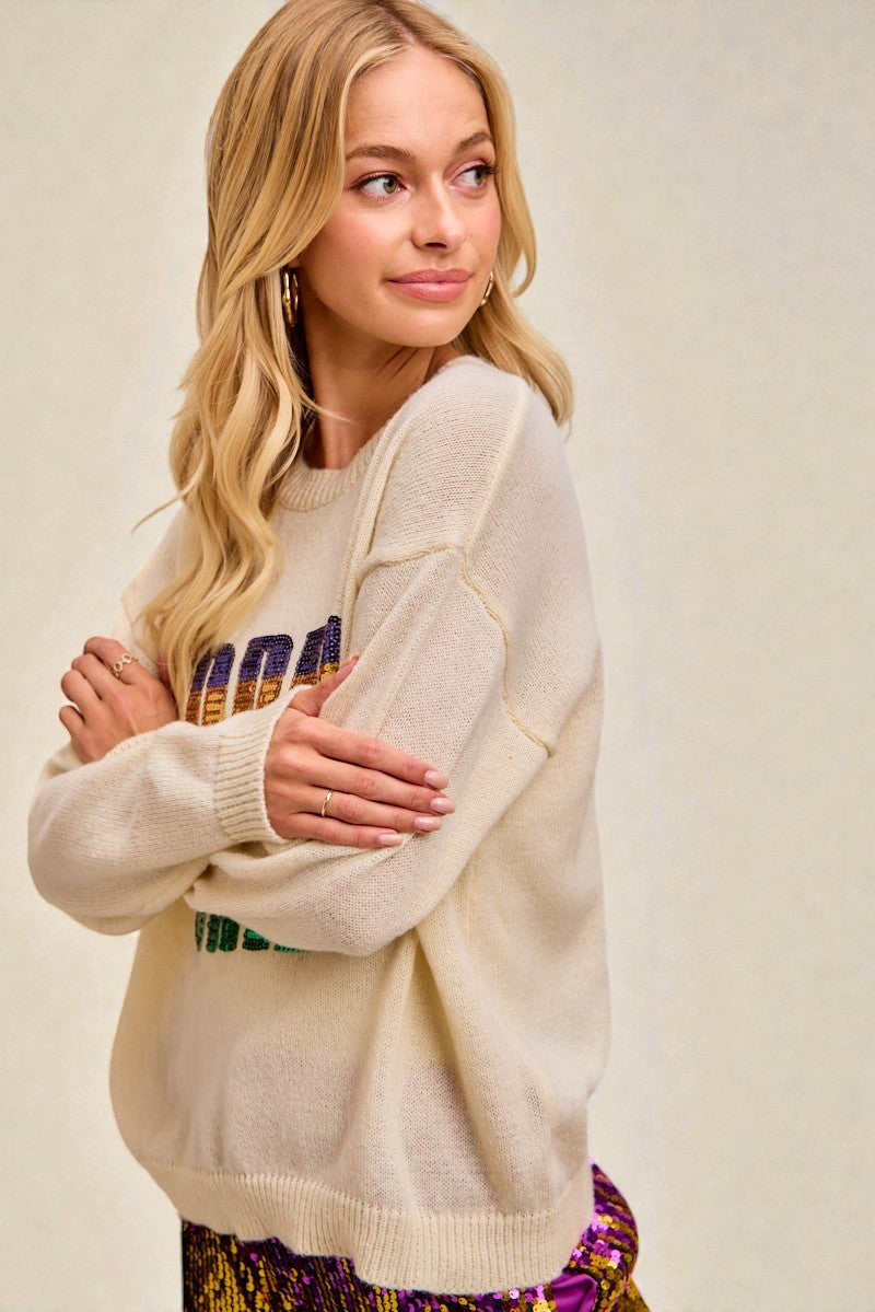 Woman wearing a cream sweater with colorful text design on a beige background