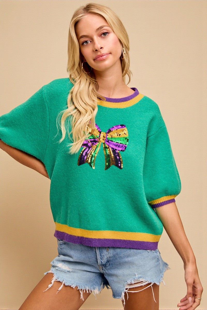Woman wearing a green sweater with a colorful bow design on a beige background