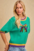 Woman wearing a green sweater with a colorful bow design on a beige background