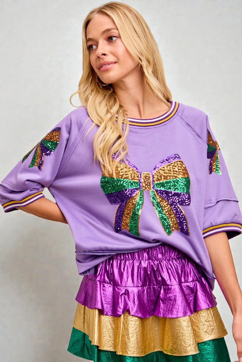 Woman wearing a purple top with colorful accents and a matching skirt against a plain background