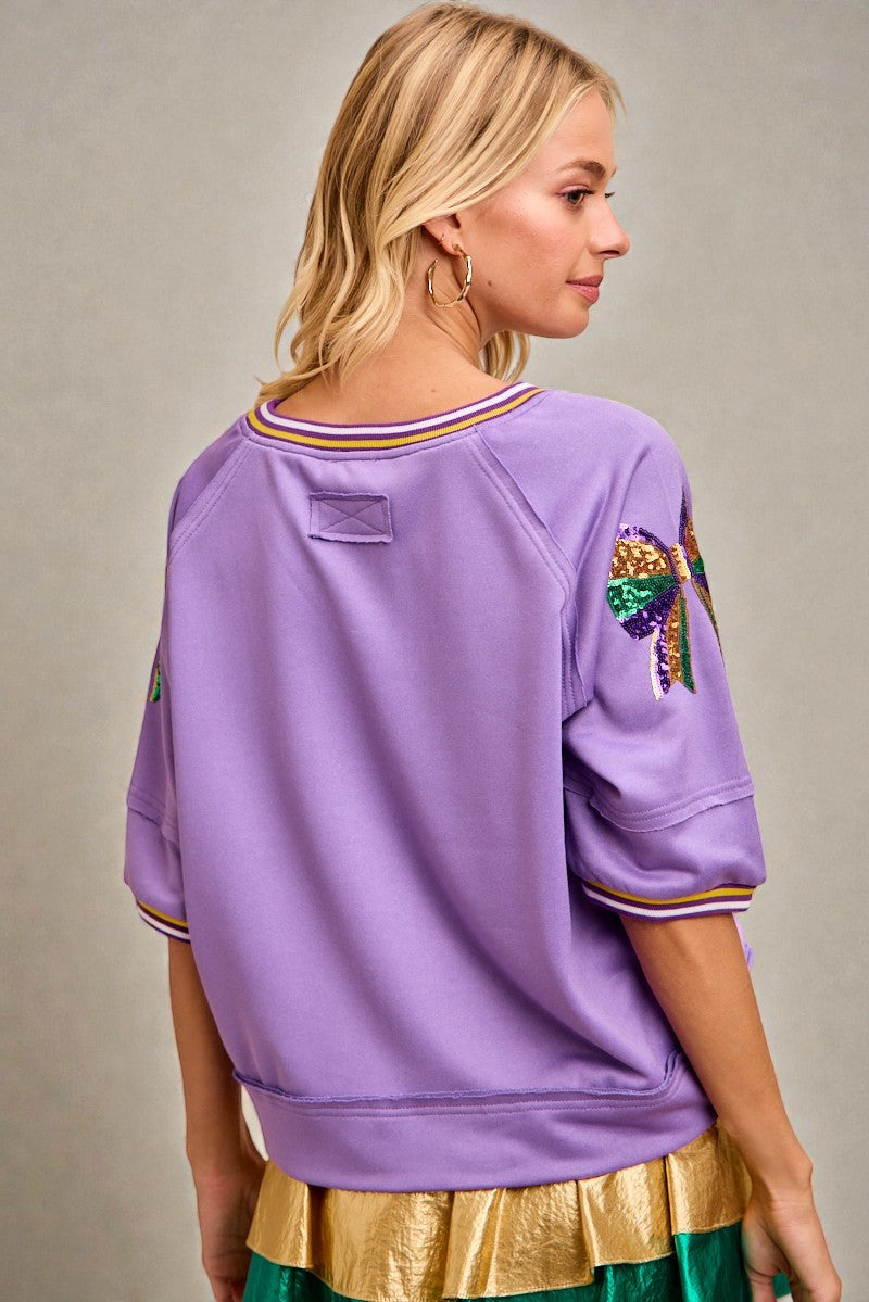 Person wearing a purple sweatshirt with colorful designs on a neutral background