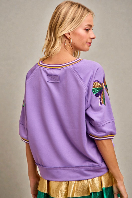 Person wearing a purple sweatshirt with colorful designs on a neutral background