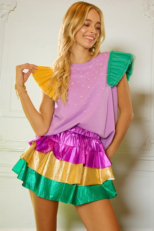 Woman wearing a colorful outfit with a purple top and multicolored skirt against a white wall.
