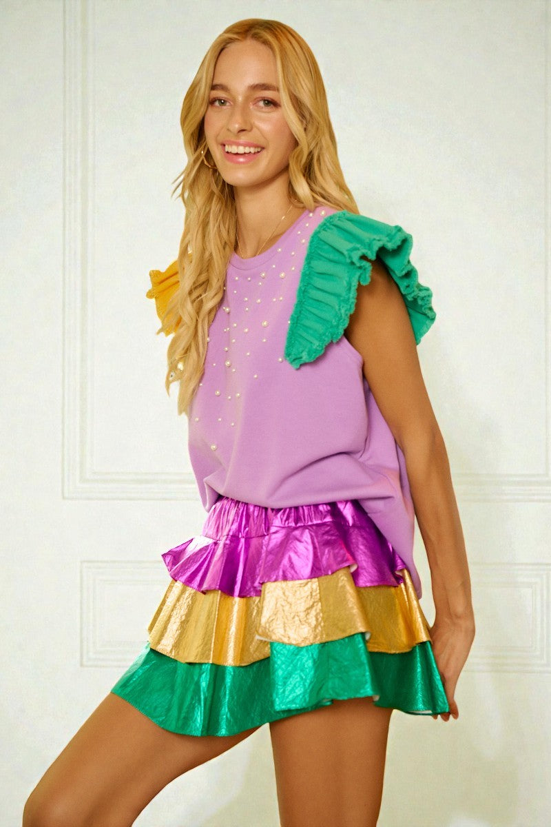 Woman wearing a colorful outfit with a purple top and green and gold skirt against a white background