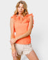Woman wearing an orange top with ruffled details and beige shorts on a white background