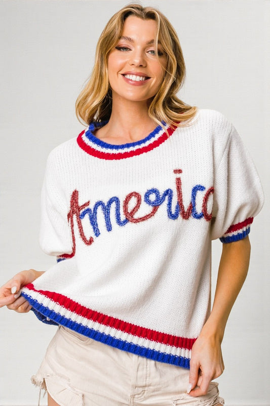 Woman wearing a white sweater with 'America' in red and blue letters on a plain background