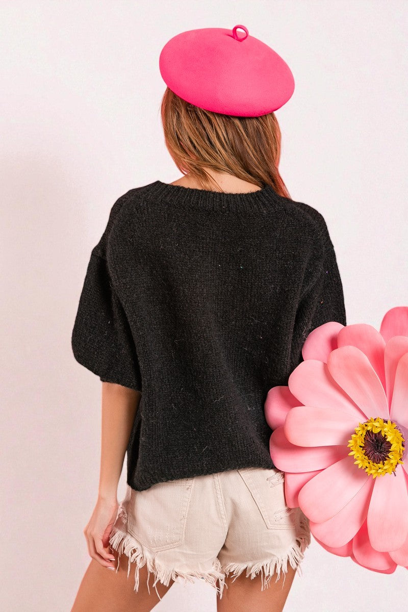 Person wearing a black sweater and pink beret with a large pink flower in the foreground on a light pink background