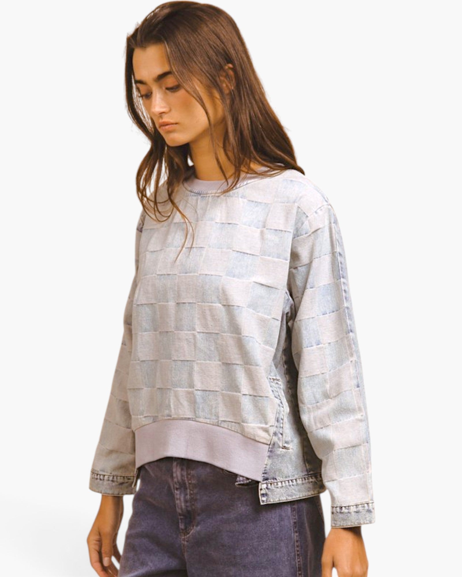 A woman wearing a light gray and white patchwork cropped sweatshirt with denim-style cuffs and hem, paired with dark jeans, against a plain white background.