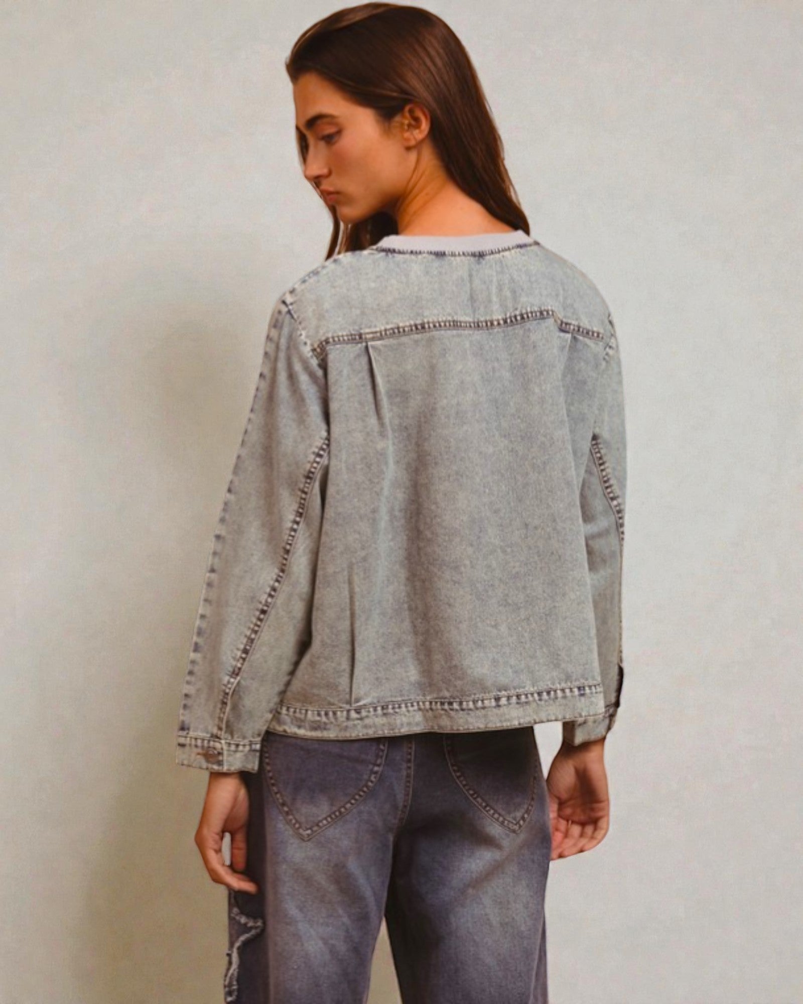 Person wearing a light blue denim jacket and jeans against a plain background