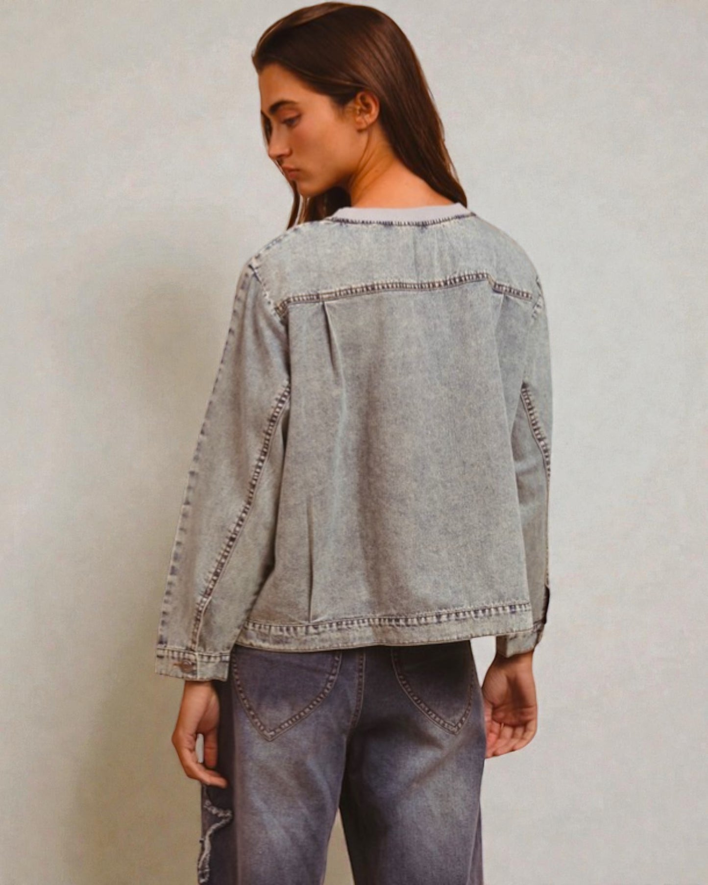 Person wearing a light blue denim jacket and jeans against a plain background