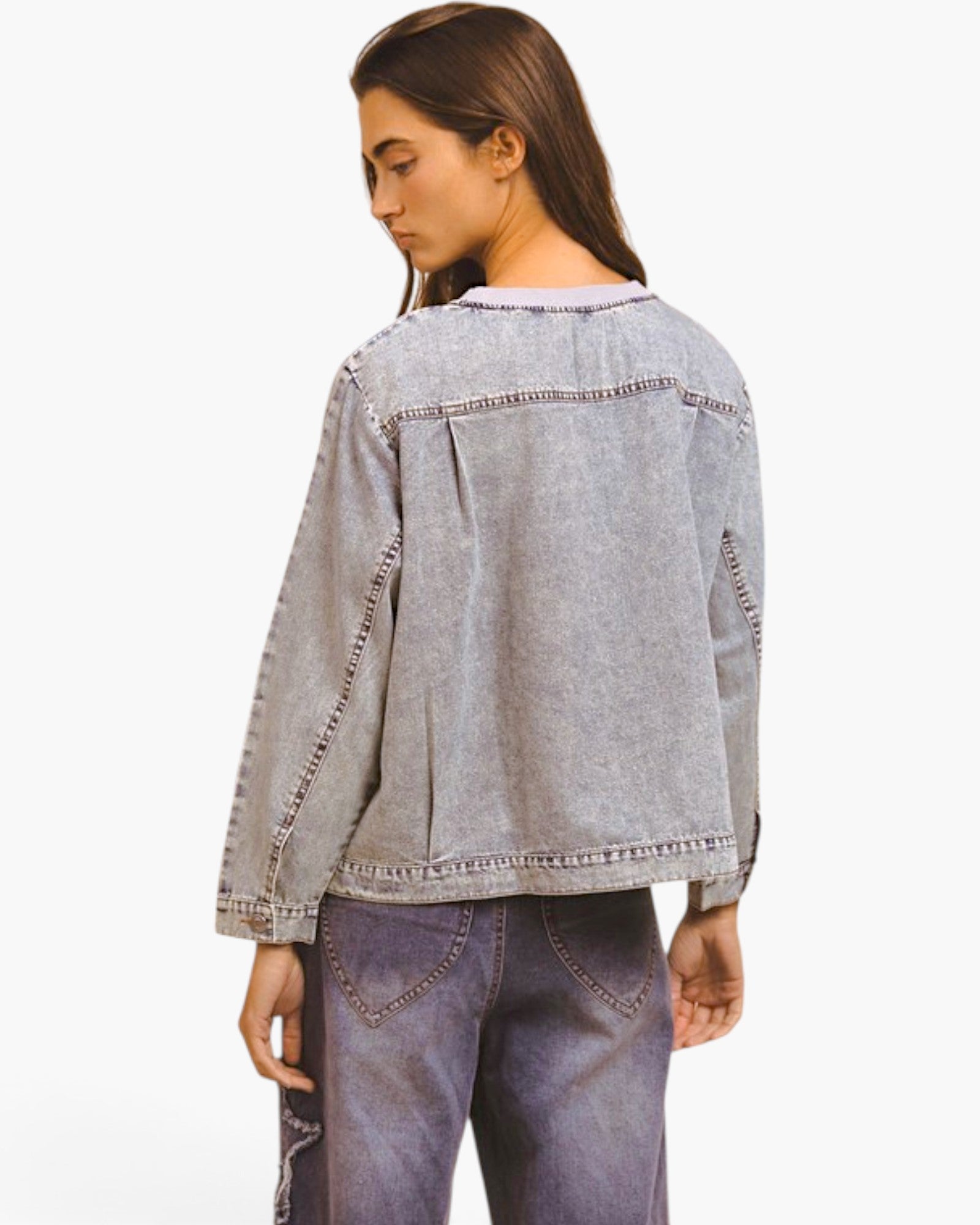 A woman shown from the back wearing a light gray washed denim jacket and matching gray jeans against a plain white studio background.