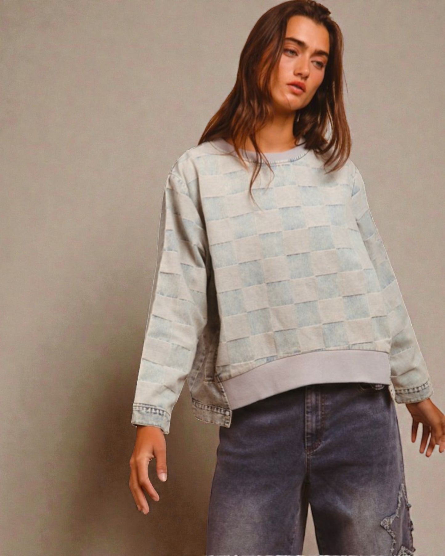 Person wearing a light blue checkered sweater and jeans against a beige background