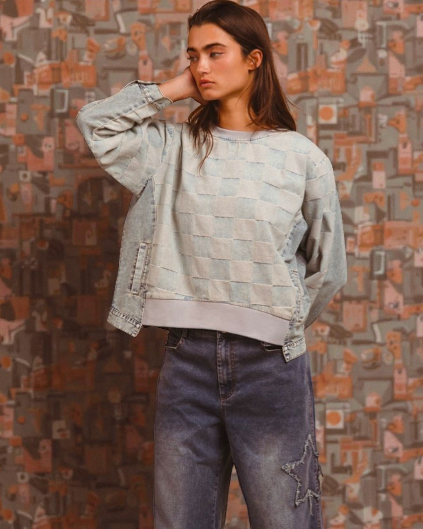 Woman wearing a patterned sweater and jeans against a textured wall.