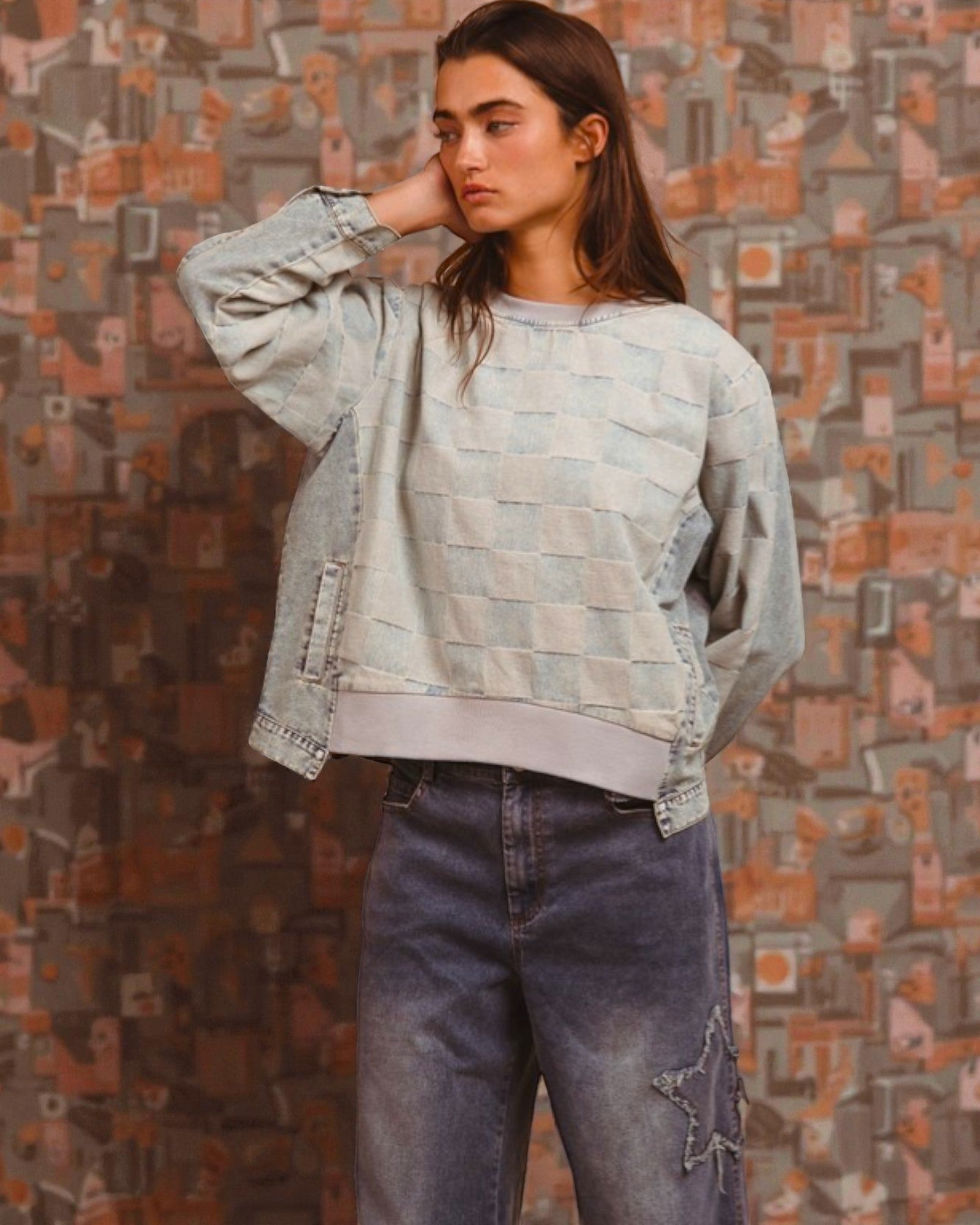 Woman wearing a patterned sweater and jeans against a textured wall.