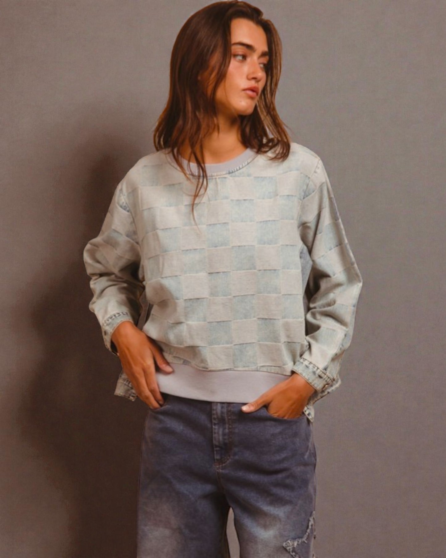 Person wearing a checkered sweater and jeans against a gray background