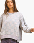A woman wearing a light-wash denim patchwork sweatshirt with a checkerboard pattern, styled with dark denim jeans against a plain white background.
