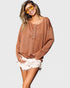 Woman wearing a brown sweater and white shorts with yellow sunglasses on a light gray background