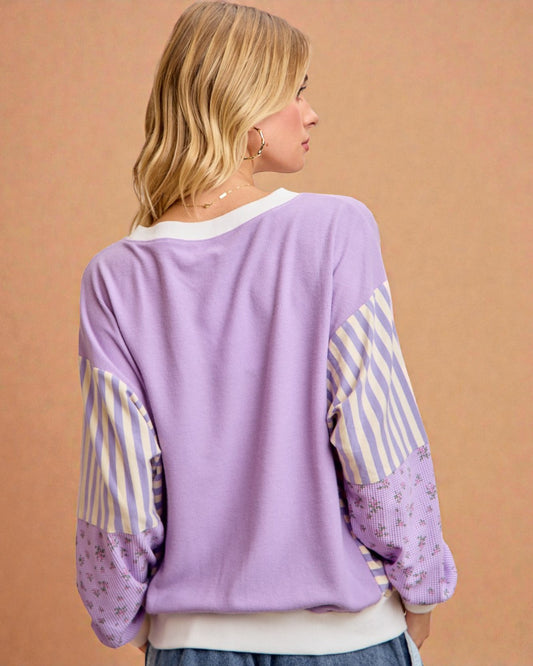 Person wearing a purple sweater with striped sleeves against a beige background