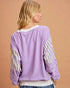 Person wearing a purple sweater with striped sleeves against a beige background