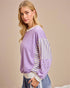 Woman wearing a purple sweater with striped sleeves against a beige background