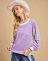Woman wearing a purple long-sleeve top with striped sleeves and a white cowboy hat on a beige background