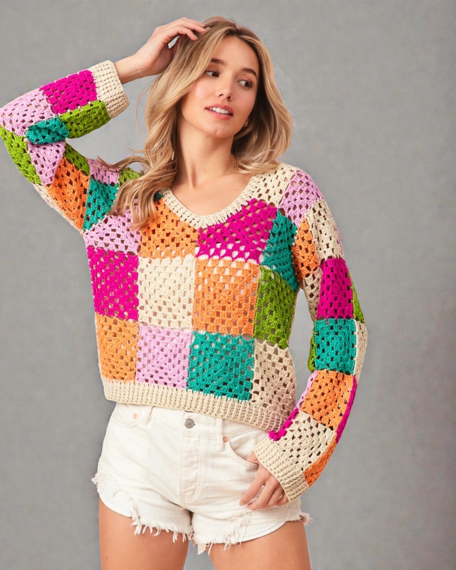 Woman wearing a colorful crochet sweater against a gray background